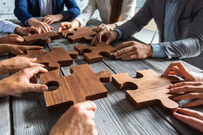 Team setzt an einem Besprechungstisch Puzzleteile zusammen